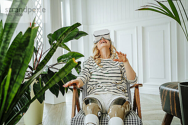 Frau mit Beinprothese spielt zu Hause ein Spiel durch eine VR-Brille