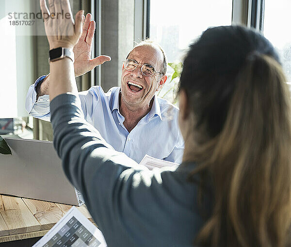 Glücklicher reifer Geschäftsmann und Kollege beim High-Five im Büro