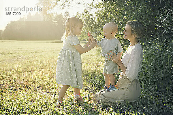 Happy mother with son and daughter playing together in nature on sunny day