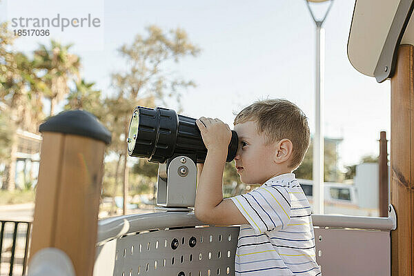 Junge blickt durch Teleskop auf Spielplatz