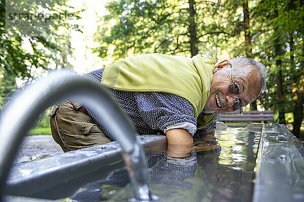 Glücklicher älterer Mann  der seine Arme in ein Kneippbecken taucht