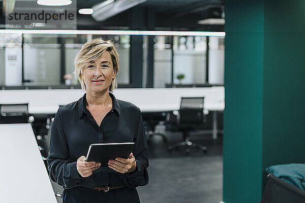 Lächelnde Geschäftsfrau hält Tablet-PC im Büro