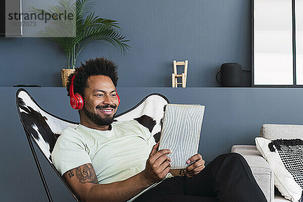Lächelnder Mann beobachtet Tablet-PC und entspannt sich zu Hause auf einem Stuhl
