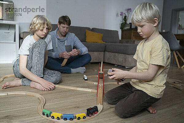 Vater und Kinder spielen zu Hause zusammen mit der Spielzeugeisenbahn