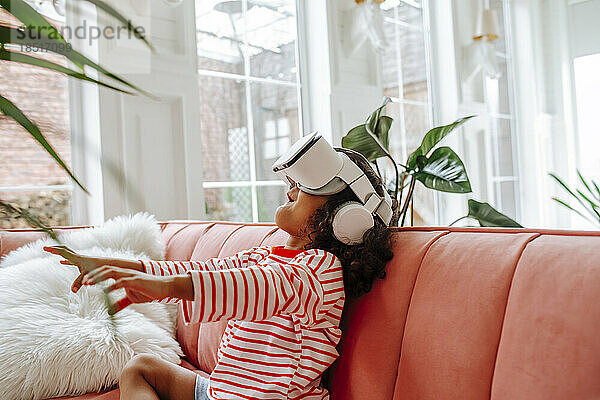Mädchen mit Virtual-Reality-Simulator gestikuliert und sitzt zu Hause auf dem Sofa