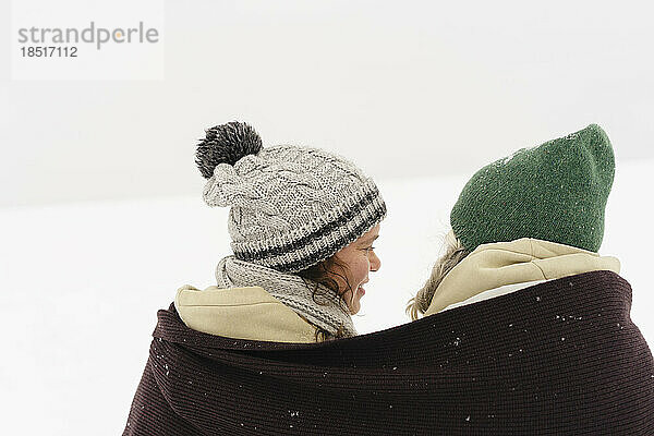 Fröhliche Freunde  die in einen Schal gehüllt sind und auf den Schnee schauen