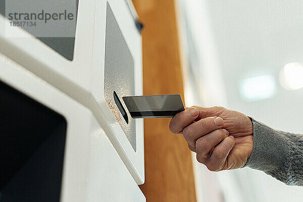 Hände eines Mannes  der eine Karte in einen Geldautomaten einführt