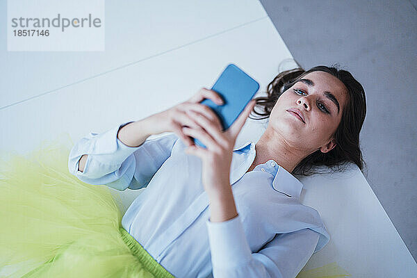 Businesswoman using smart phone lying on desk