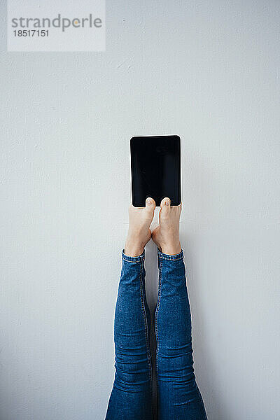 Frau hält Tablet-PC mit Zehen vor Wand