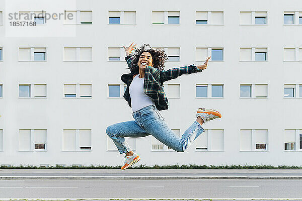 Fröhliche junge Frau springt vor Gebäude