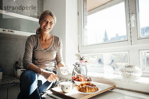 Glückliche Frau frühstückt auf der Küchentheke am Fenster