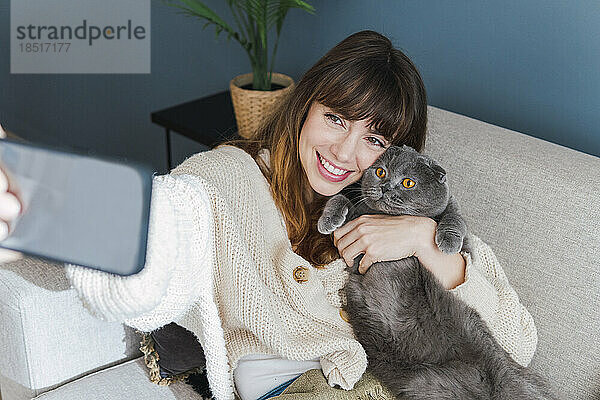 Glückliche Frau macht Selfie mit Katze  die zu Hause auf dem Sofa sitzt