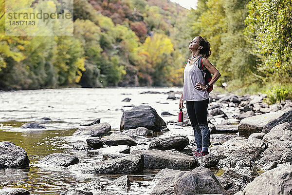 Frau mit der Hand auf der Hüfte genießt die Natur in der Nähe des Flusses