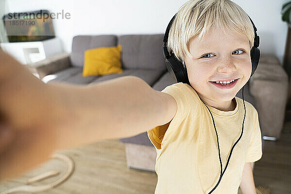 Lächelnder blonder Junge mit Kopfhörern  der zu Hause ein Selfie macht