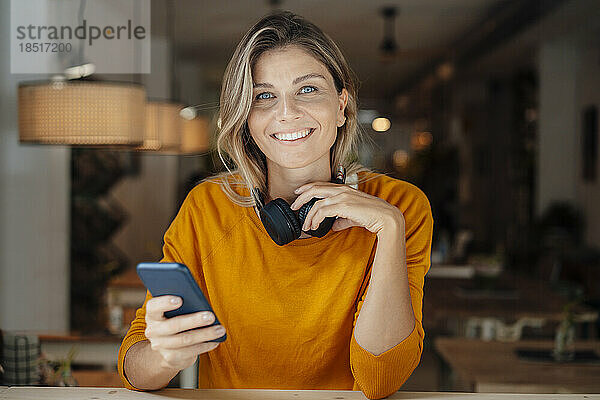 Glückliche Frau mit Smartphone sitzt im Café
