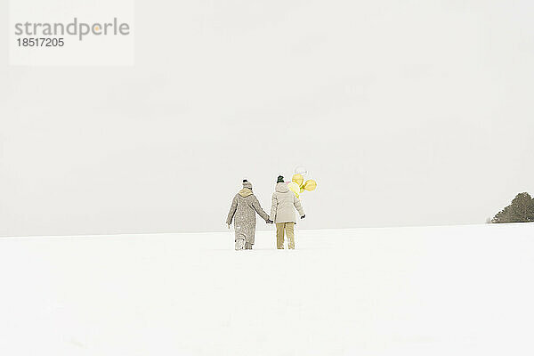 Freunde mit Luftballons laufen im Schnee