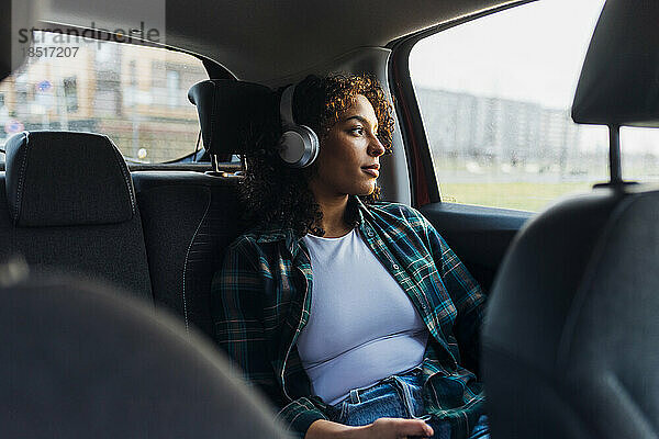 Nachdenkliche Frau trägt Bluetooth-Kopfhörer im Auto