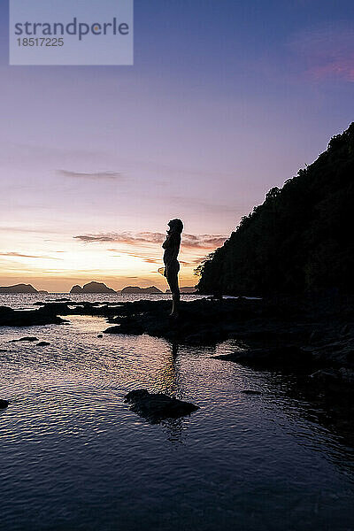 Silhouette einer Frau  die auf einem Felsen am Strand steht