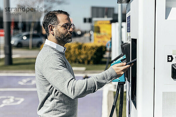 Mann bezahlt per Smartphone an der Autoladestation