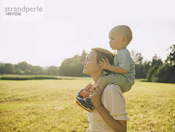 Mother carrying son on shoulders in nature on sunny day