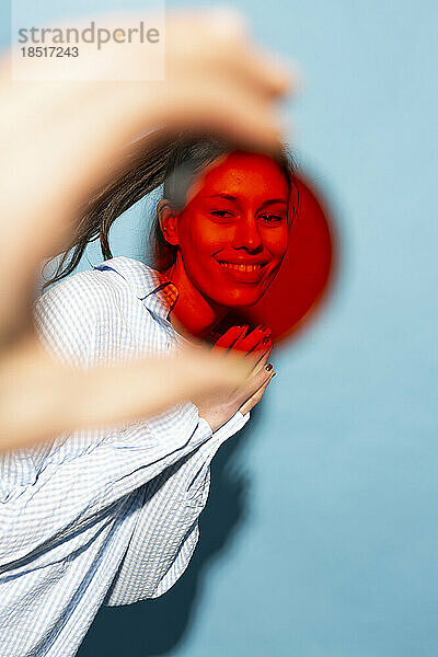 Lächelnde Frau durch roten Linsenfilter vor blauem Hintergrund gesehen