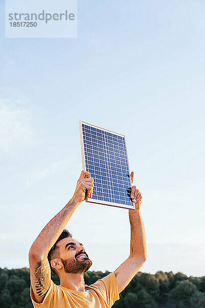 Lächelnder Mann  der an einem sonnigen Tag ein Solarpanel anhebt