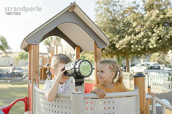 Smiling girl with brother looking through telescope
