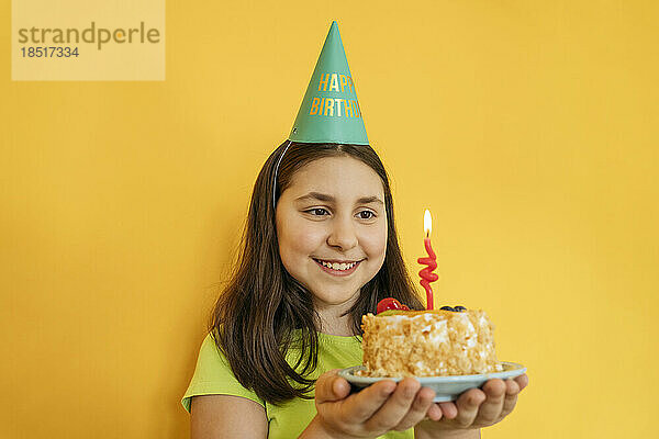 Lächelndes Mädchen hält Geburtstagstorte vor gelbem Hintergrund