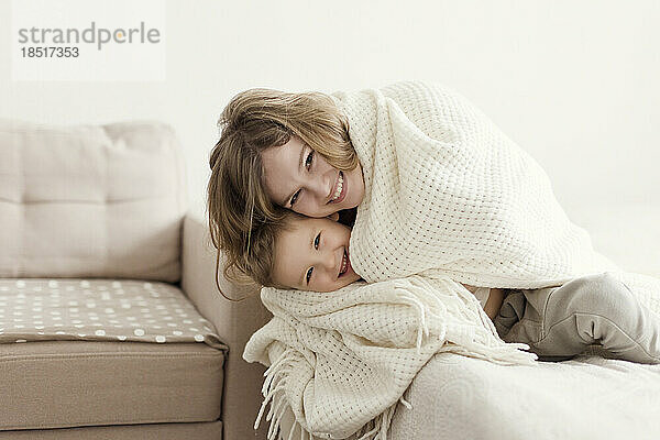 Glückliche Mutter und Sohn  zu Hause in eine Decke gehüllt auf dem Sofa