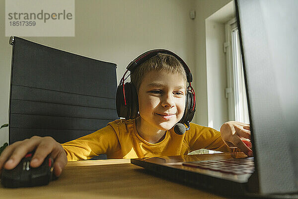 Lächelnder Junge mit Headset  der Videospiele auf dem Laptop spielt