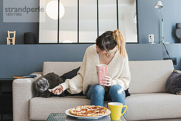 Frau füttert Katze  die zu Hause auf dem Sofa sitzt  mit Popcorn