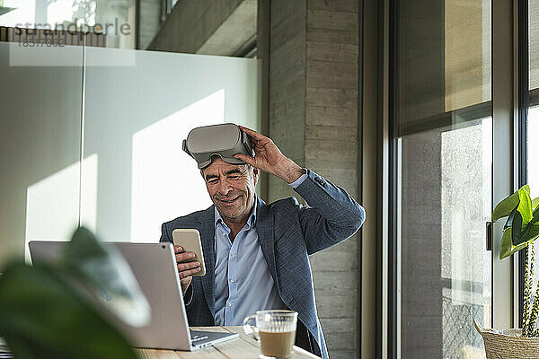 Reifer Geschäftsmann mit VR-Brille nutzt Smartphone im Büro