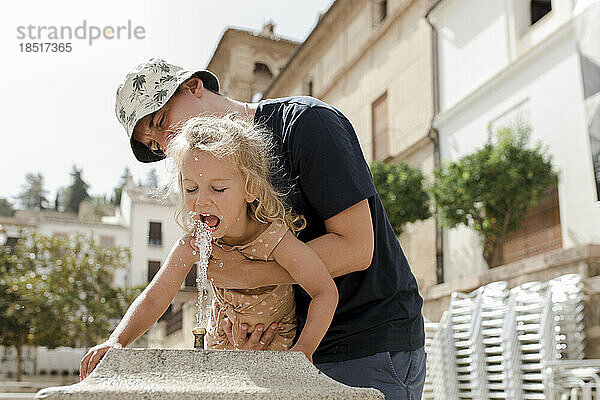 Vater und Tochter trinken Wasser aus Brunnen