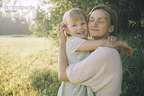 Lächelnde Mutter umarmt ihre Tochter an einem sonnigen Tag in der Natur