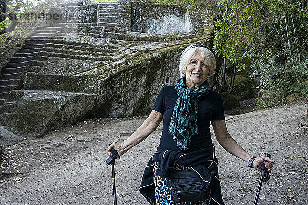 Lächelnde ältere Frau steht mit Spazierstöcken an der etruskischen Pyramide von Bomarzo