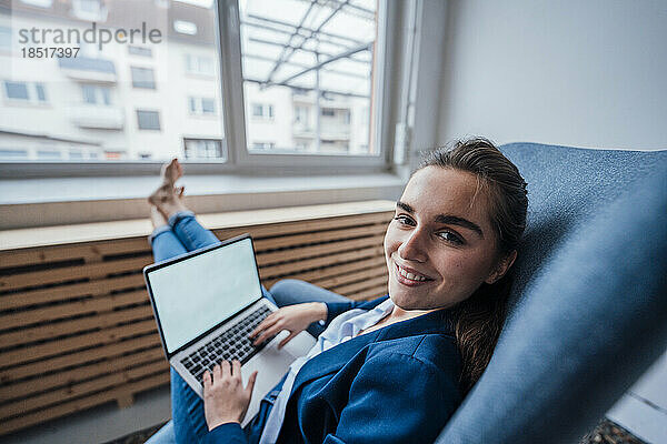 Glückliche junge Geschäftsfrau sitzt mit Laptop im Büro
