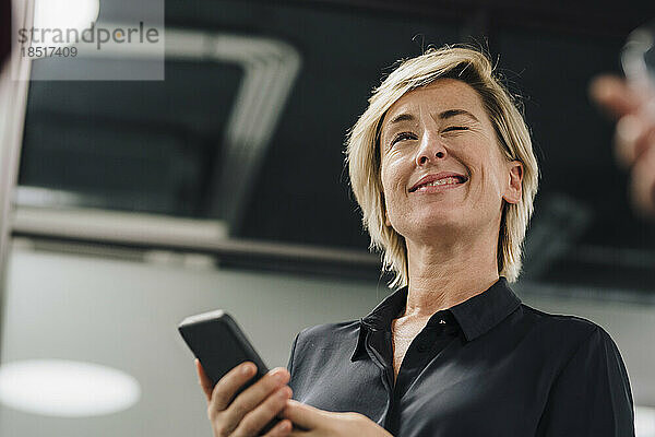 Verspielte Geschäftsfrau mit Smartphone zwinkert im Büro