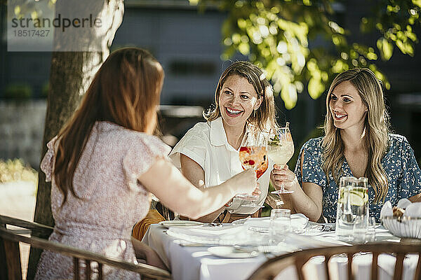 Happy female friends toasting drinks sitting at table in restaurant