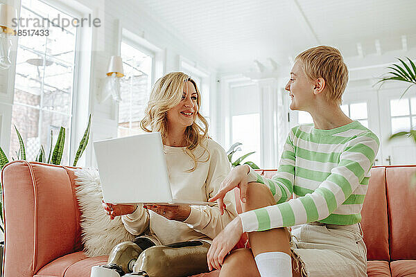 Lächelnde Frau von einem Freund mit Behinderung  der zu Hause einen Laptop hält