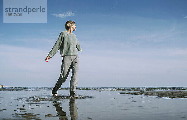 Frau mit ausgestreckten Armen läuft am Strand entlang