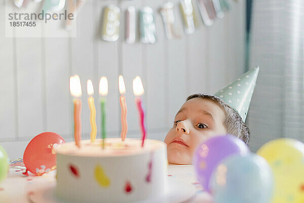 Verspielter Junge blickt auf Geburtstagstorte mit Kerzen