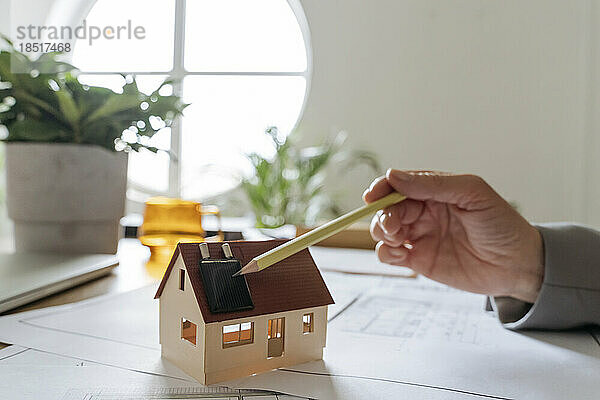 Hand eines Immobilienmaklers mit Musterhaus und Zeigestift auf Solarpanel