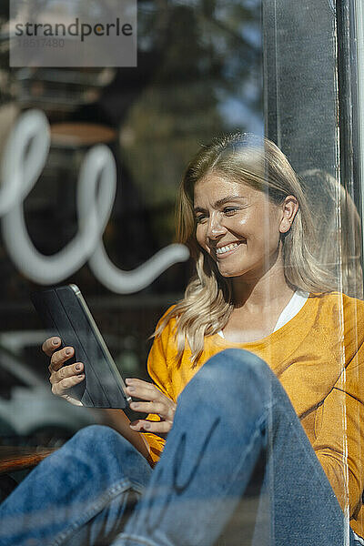 Glückliche Frau sitzt mit Tablet-PC am Fenster im Café