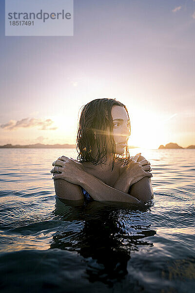 Nachdenkliche Frau umarmt sich bei Sonnenuntergang im Meer