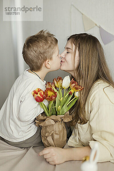 Son kissing mother with bouquet of tulips at home