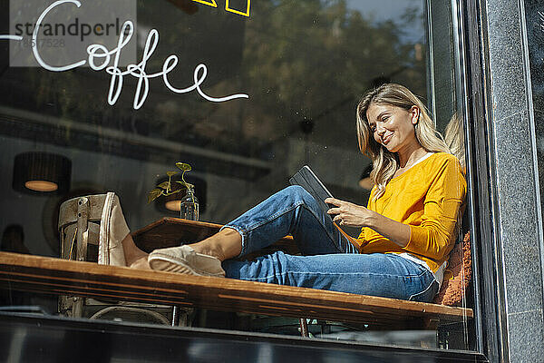 Lächelnde Frau benutzt Tablet-PC im Café  gesehen durch Glas