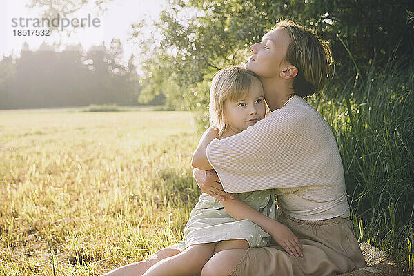 Mother hugging daughter sitting in nature