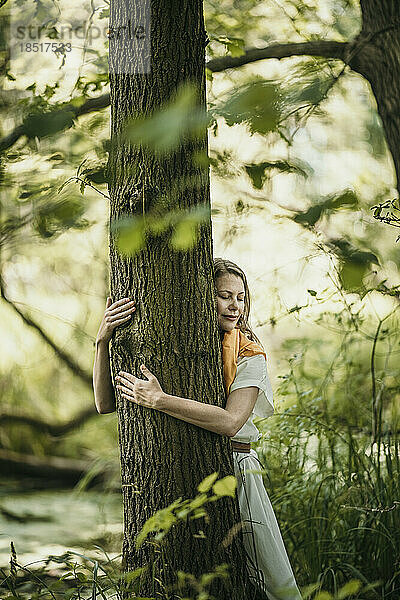Mature woman with eyes closed embracing tree in forest