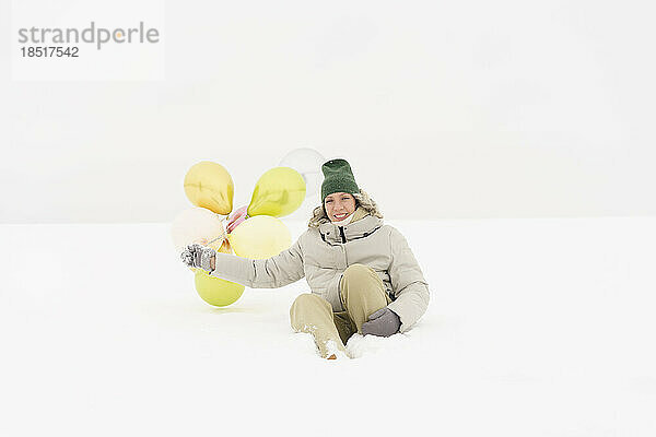 Glückliche Frau mit Luftballons  die Spaß im Schnee hat