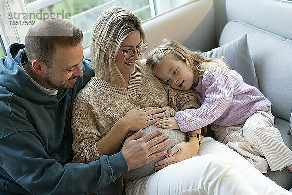 Vater und Tochter berühren zu Hause den Bauch einer schwangeren Frau